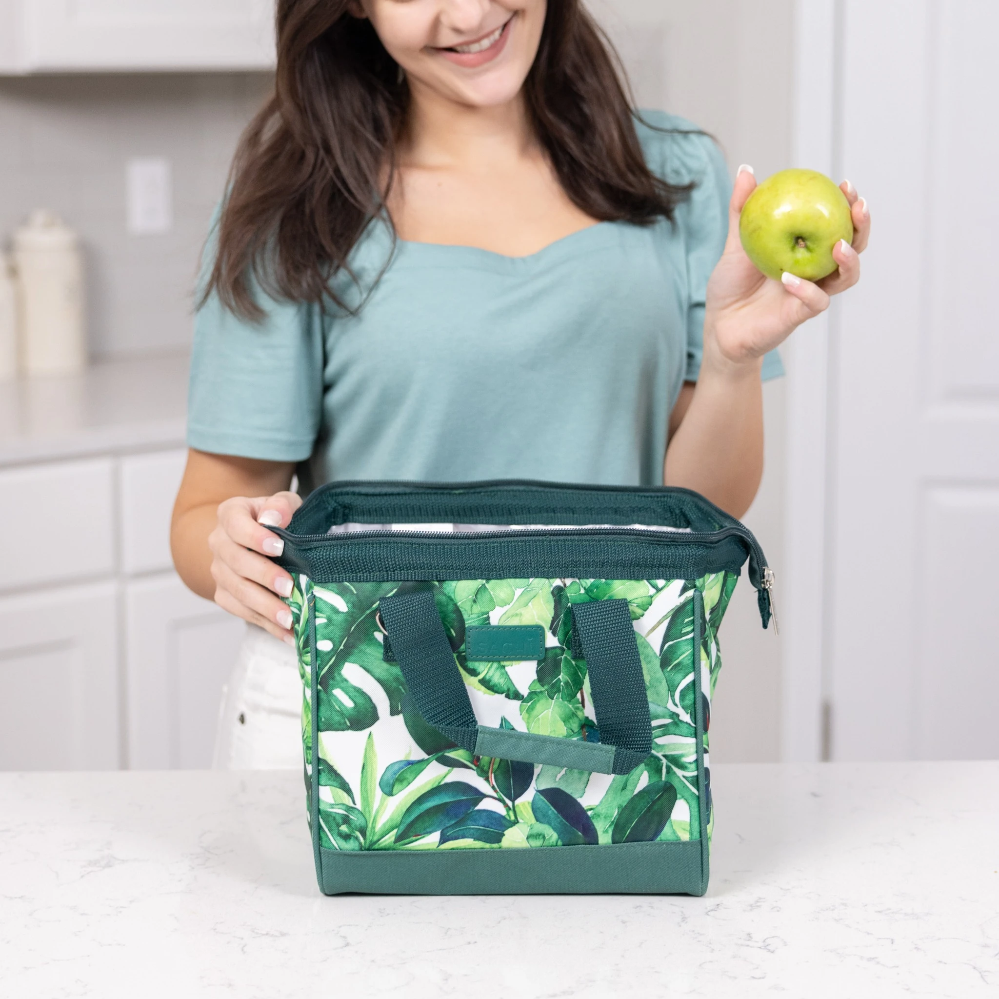 Woman packing a SACHI Style 034 Tropical Green Leaf insulated lunch bag